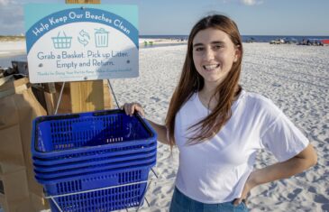 Hannah Smith stands for a photo next to a display of beach cleaning baskets. The South Walton High School student started a program that provides free baskets to beach goers who want to help keep the beach clean.